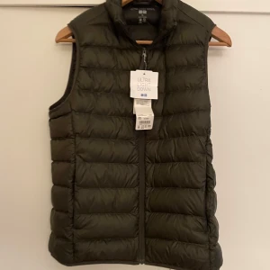 Olivgrön dunväst från Uniqlo XS - Säljer en oanvänd olivgrön, ultralätt dunväst från Uniqlo i storlek Herr XS. Västen har quiltad design, hög krage och dragkedja framtill. Perfekt att slänga över en hoodie eller tröja när det är kyligt ute.