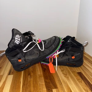Nike X Off-White Air Force 1 Mid sneakers Black - Unika Nike Air Force 1 x Off-White i svart med coola detaljer som färgglada taggar på sulan, vita och svarta snören samt genomskinlig swoosh. Skorna har broderad AIR-logga på plösen och orange detaljer. Perfekt för dig som vill sticka ut.