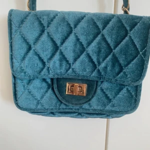  blå axelväska i sammet - Snygg quiltad axelväska i blå sammet med guldfärgat vridlås.