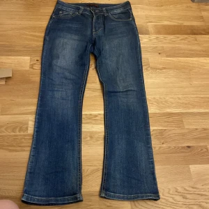 Vintage Lågmidjade bootcut jeans  - Snygga blå bootcut jeans från Place du Jour i storlek 36. Klassisk femficksmodell med en liten stjärndetalj på bakfickan. Jeansen är i stretchigt material med 97% bomull och 3% elastan för skön passform.