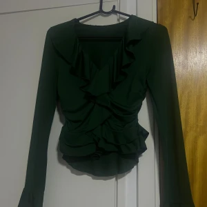 Mörkgrön blus med volangdetaljer - Supersnygg mörkgrön blus med v-ringning och volanger längs halsringningen och framtill.✨✨