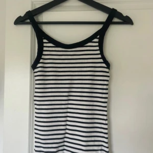 Randigt linne i vitt och marinblått - Snygg ribbat linne med marinblåa och vita horisontella ränder. Toppen har axelband och rundad halsringning med svarta kanter. Perfekt för en chill och stilren look. Materialet känns mjukt och stretchigt.