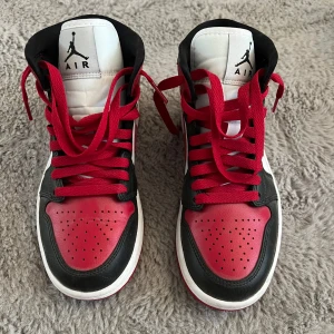 Nike Air Jordan 1 High röd/svart/vit - Säljer ett par Nike Air Jordan 1 High i klassisk röd, svart och vit färg. Skorna har högt skaft, röda snören och perforerad tå. Ikonisk Jumpman-logga på plösen och vingar på sidan. Tillverkade i skinn och syntet, perfekt för dig som gillar streetstyle. De är endast använda en gång så de är iprincip i nyskick! 