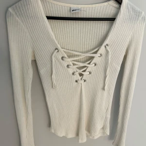 Ribbad vit tröja med snörning Gina Tricot - Supersnygg ribbad vit långärmad tröja från Gina Tricot med djup v-ringning och cool snörningsdetalj framtill. Perfekt till jeans eller kjol för en trendig look. Mjuk och stretchig, sitter riktigt snyggt på kroppen.