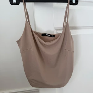 Beige linnetopp  - Säljer en stilren beige linnetopp från Bik Bok med tunna, justerbara axelband och lätt draperad halsringning. Toppen är i mjukt, stretchigt material och har en enkel, clean look som passar perfekt till jeans eller kjol. Har aldrig blivit använd så är i perfekt skick!