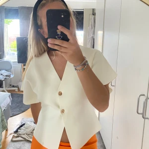 Vit v-ringad blus från Zara - Superfin vit blus från Zara med v-ringning och två snygga knappar framtill. Modellen har korta, vida ärmar och en lätt strukturerad känsla i tyget. Perfekt till både jeans och kjol för en clean look. Aldrig använd! Lappen sitter kvar