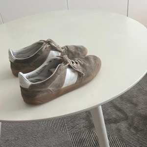 Beige sneakers från BOSS i mocka - Snygga beige sneakers från BOSS med vit detalj på sidan och gummisula. Skorna har snörning och är tillverkade i mocka och skinn, vilket ger en lyxig känsla. Perfekta för dig som gillar stilrena och klassiska sneakers med en modern touch.
