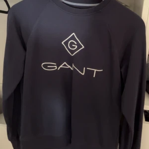 Mörkblå sweatshirt från GANT - Snygg mörkblå sweatshirt från GANT med vit logga framtill. Klassisk rund halsringning och långa ärmar. Perfekt för dig som gillar stilrena och bekväma plagg med en sportig touch. Materialet känns mjukt och skönt mot huden.