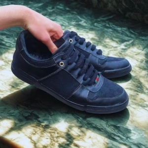 Gucci skor - Logga i guld på hälen och rödgrön detalj på snörningen. Skorna har svarta skinn- och textilpaneler, svarta snören och röd sula med Gucci-tryck undertill. 100% autentiska, kommer med dustbag. Liten slitning på ena textilen men annars inga defekter förutom lite tecken på användning.