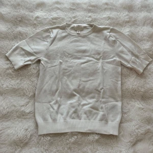 Vit stickad kortärmad tröja - Superfin vit stickad tröja med korta ärmar och rund hals. Tröjan har en clean och enkel look med ribbade muddar i nederkant och vid ärmslut. Perfekt till vår och sommar för en fräsch och stilren vibe.