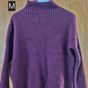 Vinröd ribbad stickad tröja M - Mysig vinröd stickad tröja med ribbat mönster och hög hals. Tröjan har lång ärm och en relaxed fit som passar perfekt till lager-på-lager. Perfekt för kyliga dagar när du vill vara både bekväm och snygg.