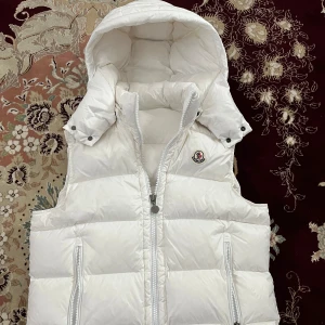 Vit dunväst från Moncler med huva - Säljer en snygg vit dunväst från Moncler med avtagbar huva och dragkedja framtill. Västen har två praktiska fickor med dragkedja och ikonisk Moncler-logga på bröstet. Perfekt för lager-på-lager och riktigt clean look.