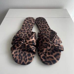 Leopardmönstrade sandaler med rosett - Snygga sandaler med leopardmönster i bruna och svarta toner. De har en stor rosett framtill som ger en trendig och lekfull vibe. Perfekta för sommardagar när du vill sticka ut lite extra. Materialet känns mjukt och svalt mot foten. Små i storleken så passar någon som bär 39