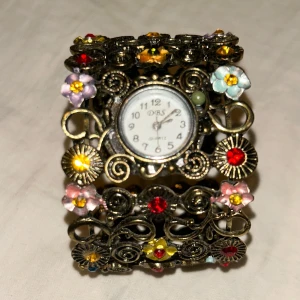 Blommig armbandsklocka  - Supersnygg arbandsklocka i metall med blomdetaljer. Batterier behöver bytas. Den har gått sönder på ett ställe (se bild 4)
