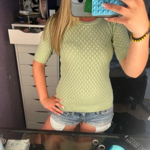 Ljusgrön stickad topp med kort ärm - Superfin ljusgrön stickad topp med korta ärmar och snyggt hålmönster över hela tröjan. Sitter tajt och har ribbade muddar vid ärmslut och nederkant. Perfekt till jeansshorts eller kjol för en fräsch look.