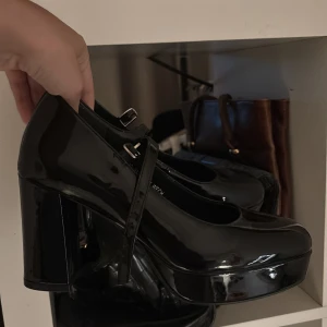 Svarta pumps med platå - Snygga svarta pumps med hög klack och platåsula. Skorna har en rund tå, lackad finish och justerbart spänne över foten.  Aldrig använda