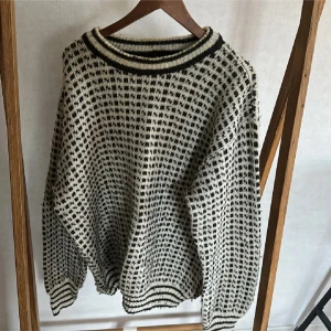 Mönstrad stickad tröja från Norcewool - Säljer en stickad tröja från Norcewool i svart och vit med rutigt mönster. Tröjan har ribbade muddar och krage med svarta ränder, samt långärmad passform. Perfekt för dig som gillar retrovibbar och vill ha något unikt i garderoben.