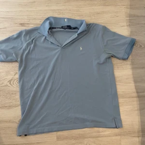 Ljusblå pikétröja från Polo Ralph Lauren - Snygg ljusblå pikétröja från Polo Ralph Lauren med klassisk krage och korta ärmar. Tröjan har den ikoniska broderade loggan på bröstet och är gjord i mjuk bomull. Perfekt för en clean och stilren look.