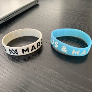 Marcus & Martinus silikonarmband - Två silikonarmband från Marcus & Martinus, ett i vitt med svart text och ett i ljusblått med vit text. Båda har tydlig logga och text runt hela bandet. Perfekt accessoar för fans som vill visa sitt stöd för sina idoler.