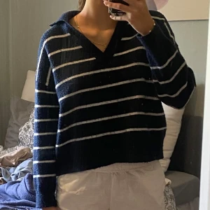 Mörkblå randig stickad tröja - Mysig mörkblå stickad tröja med vita horisontella ränder och krage. Tröjan har v-ringning och långa ärmar, perfekt för lager-på-lager. 