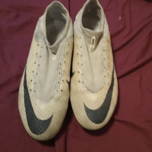 Nike mecurial pros - Snygga fotbollsskor från Nike i vitt med svarta detaljer och stor Swoosh-logga. Skorna har låg profil, plös med elastisk mudd och mönstrad ovandel i syntetmaterial. Yttersulan har fasta dobbar för bra grepp på planen. Perfekta för dig som vill sticka ut på matchen.