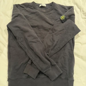 Svart sweatshirt från Stone Island - Svart sweatshirt från Stone Island med klassisk rund hals och ribbade muddar. Ikonisk logga på vänster ärm. Mjuk bomullskänsla och relaxed fit, perfekt för en clean och stilren look.