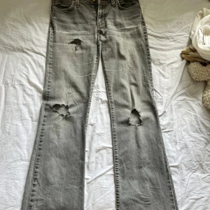 Gråa bootcut  jeans med slitningar - Säljer ett par gråa bootcut jeans och snygga slitningar vid knäna. Jeansen har klassisk femficksdesign, normal midja och är i ett mjukt denimtyg. Perfekta för en avslappnad och trendig look. Det står ingen storlek i men jag är 163 och de passar väldigt bra så skulle säga 34/36. Hålen är gjorda själva