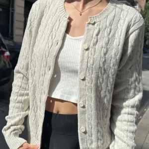 Ljusbeige kabelstickad kofta Brandy Melville - Superfin grå kabelstickad kofta från Brandy Melville med rund halsringning och knappar framtill. Mjuk och mysig, perfekt till lager-på-lager. Långärmad och ribbade muddar för extra comfy känsla. 53 cm length 48 cm bust