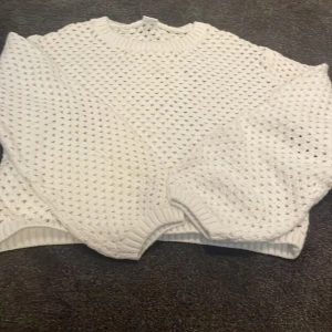 Vit stickad tröja från Lindex - Vit stickad tröja från Lindex med snyggt hålmönster och ribbade muddar vid ärmslut och hals. Perfekt för lager-på-lager och ger en chill vibe till din outfit. Passar dig som gillar en klassisk men trendig look.