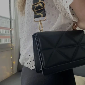 väska - Superfin svart handväska med svart och guldigt band. Säljer då jag rensar ut väskor 🫶🏼