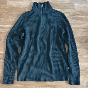 Mörkblå ribbad polotröja med half zip - Snygg mörkblå ribbad polotröja med halv dragkedja framtill. Tröjan har lång ärm och hög krage, perfekt för lager-på-lager. Materialet är stretchigt och sitter skönt mot kroppen. Enkel att matcha med både jeans och kjol.
