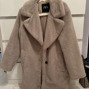 Beige teddyjacka från Zara XS - Säljer en fluffig teddyjacka från Zara i beige färg, storlek XS. Jackan har bred krage, två stora fickor och stängs med svarta knappar framtill. Perfekt för dig som vill ha en mysig och trendig look under kyliga dagar. Jackan är i nytt skick och har bara använts en gång! ❤️