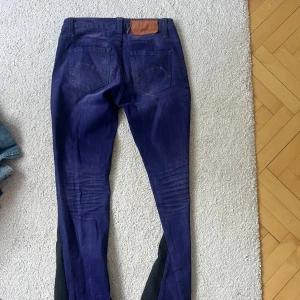 Mörkblå bootcut jeans  - Snygga mörkblå jeans från One Green Elephant med cool rosa insida i midjan och klassisk femficksdesign. Jeansen har raka ben med svarta paneler längs sidorna och detaljerade sömmar på bakfickorna. Perfekt för dig som vill sticka ut med färg och stil.
