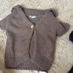 Brun stickad kofta från Zara - Mysig brun stickad kofta från Zara med korta ärmar och v-ringning. Koftan har en enkel knapp framtill och bred ribbad kant vid ärmslut och nederkant. Perfekt att slänga över en t-shirt för en chill look. Helt oanvänd