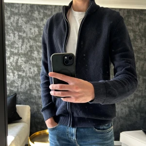 Mörkblå stickad kofta - Säljer en mörkblå stickad kofta med grov ribbad struktur och hel dragkedja framtill. Använd 2 gånger. Bara att skriva vid frågor! 