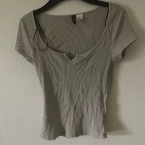 Beige ribbad topp med v-ringning - Säljer en beige ribbad topp från Divided med korta ärmar och snygg v-ringning. Toppen har en figurnära passform och är tillverkad i mjuk bomullsmix. Perfekt att matcha med jeans eller kjol för en enkel och stilren look.