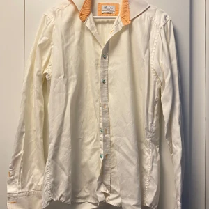 Vit Stenströms skjorta med orange krage - Vit skjorta från Stenströms med slimline-passform. Kragen och insidan av manschetterna har orange och vit rutigt tyg, vilket ger en snygg kontrast. Skjortan har turkosa knappar och är tillverkad i mjuk bomull. Perfekt för dig som gillar detaljer och stil.