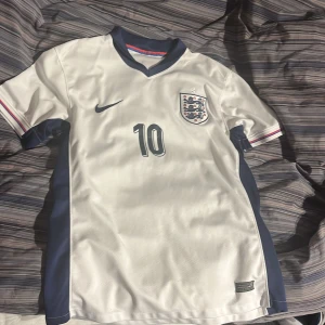 Bellingham England tröja - England tröja med Jude Bellingham på ryggen. Köpt i England så den är äkta, endast en defekt vilket är en liten del av trycket på ryggen. Priset är ej hugget i sten