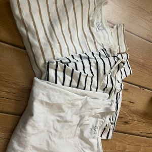 3-pack randiga och vit t-shirt - Säljer tre t-shirts i fräsch stil: en vit med beige ränder från Lindex, en vit med svarta ränder och en helvit från Basic You. Alla har rund hals och är kortärmade, gjorda i mjuk bomull, varav två i ekologisk kvalitet. Perfekt för chill och enkel look.