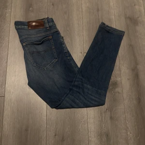 Tiger of Sweden jeans - Snygga blå jeans från Tiger of Sweden med klassisk femficksdesign och brunt läderpatch bak i midjan. Jeansen har en rak passform och subtila slitningar framtill för en cool look. Perfekta för dig som gillar stilrena och tidlösa jeans med lite edge.