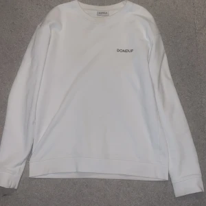 Vit sweatshirt från Dondup - Säljer en clean vit sweatshirt från Dondup med diskret logga på bröstet. Tröjan har rund hals, långa ärmar och är tillverkad i mjuk bomull. Perfekt för dig som gillar minimalistisk stil och italiensk design. Strl M men sitter mer som en L