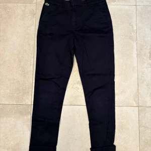 Mörkblå chinos från Lacoste - Mörkblå chinos från Lacoste. Raka ben. Sidofickor och bakfickor. Bomull. 
