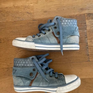 💓Blå denim sneakers från Mustang💓 - Snygga höga sneakers från Mustang i ljusblå denim med coola utskurna detaljer och snörning. Skorna har vit sula med blå rand, bruna detaljer och Mustang-logga baktill. Perfekta för dig som gillar streetstyle och vill sticka ut med unika detaljer.❤️