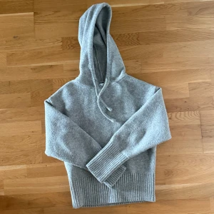 Grå stickad hoodie Zara - Populär grå hoodie från Zara i stickat material med luva och snörning. Tröjan har långa ärmar och breda ribbade muddar vid ärmslut och nederkant. Perfekt för kyliga dagar och enkel att matcha med jeans eller mjukisbyxor🩶