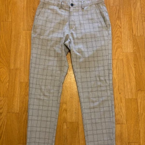 Grå rutiga kostymbyxor från Zara - Snygga grå kostymbyxor från Zara med klassiskt rutigt mönster. Byxorna har raka ben, sidfickor och hällor för bälte. Perfekta för en clean och stilren look. Materialet känns mjukt och bekvämt mot huden.