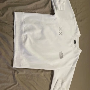 Vit sweatshirt The North Face x KAWS - Vit sweatshirt från The North Face i samarbete med KAWS. Tröjan har diskret logga och två gråa X på bröstet. Klassisk rund halsringning och långa ärmar. Mjuk bomullskänsla och relaxed fit, perfekt för en clean och stilren look. Använd 4, 5 gånger men helt ren. Storlek S män. Skickas inom 1-3 dagar.