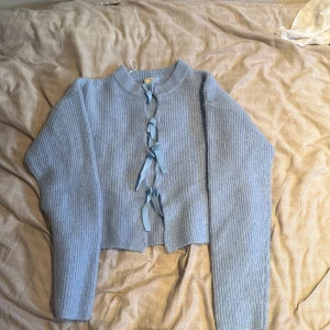 Ljusblå stickad kofta med snörning - Superfin ljusblå stickad kofta från Gina Tricot med ribbad struktur och snygga snörningsdetaljer framtill. Koftan har långa ärmar och en croppad passform som ger en trendig look. Perfekt att slänga över en topp för en chill vibe.