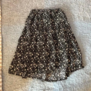 Svart blommig kjol i bomull - Svart kjol med vita små blommor.Jag har inte storlek 116 i kjolar men denna kjol kan man använda till en lång kjol blandat med en vanlig kort kjol.Den är skön och har lite volym.💕