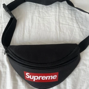 Svart Supreme magväska - Supreme magväska i svart med klassisk röd logga framtill. Väskan har justerbart band, två fack. 🔥🔥