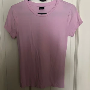 Ljusrosa t-shirt från Gina Tricot - Enkel och stilren ljusrosa t-shirt från Gina Tricot. Modellen är klassisk med rund halsringning och korta ärmar. Perfekt att matcha med jeans eller kjol för en avslappnad look.